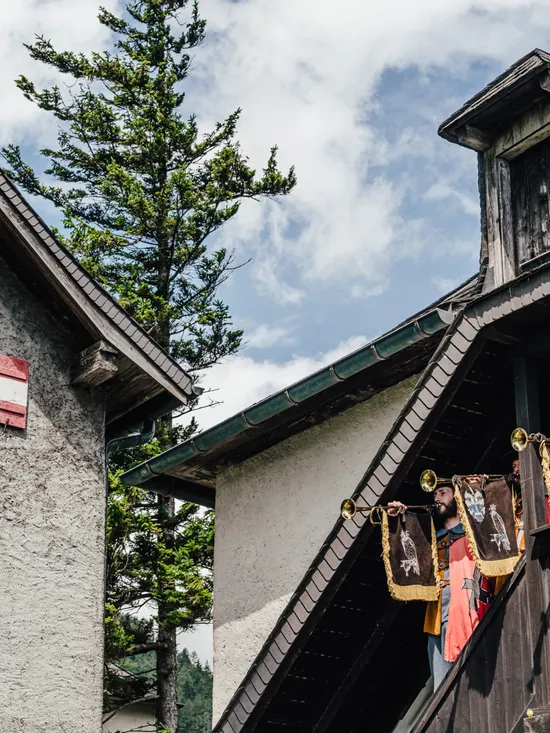 Men in traditional costumes playing herald trumpets on a wooden balcony in Alpine village