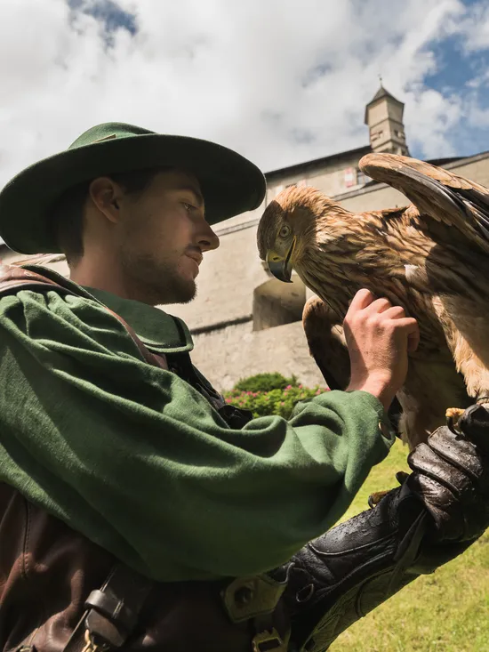 Falconiere in abito verde con aquila marrone vicino a un castello di pietra storico