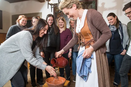 Donna in abito tradizionale versa acqua sulle mani di un'altra durante un'attività culturale di gruppo