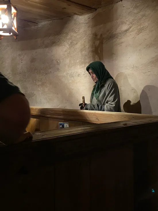 Donna in abiti medievali lavora con attrezzi sotto la luce di una lanterna in una bottega rustica