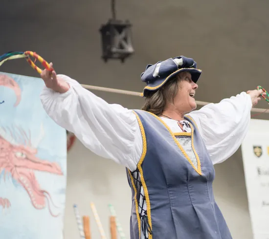 Artista in costume medievale che intrattiene con nastri a una fiera rinascimentale
