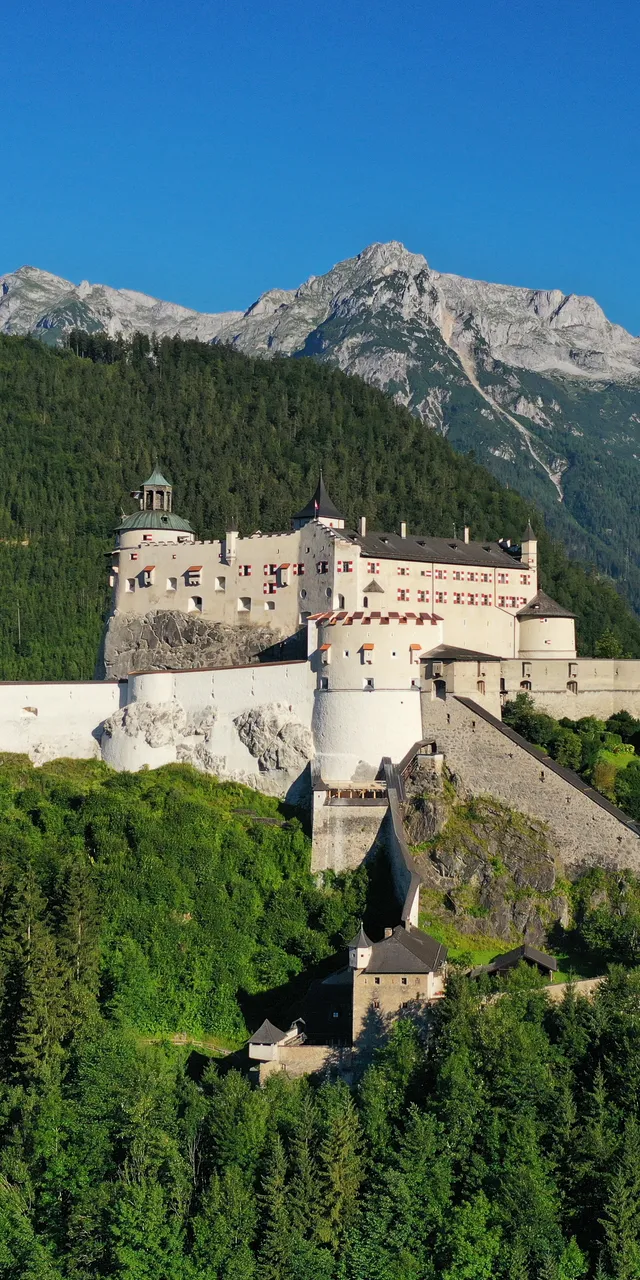 Medieval Hohenwerfen Castle surrounded by alpine forest with mountain range in the background
