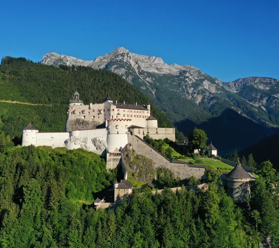 Medieval Hohenwerfen Castle surrounded by alpine forest with mountain range in the background