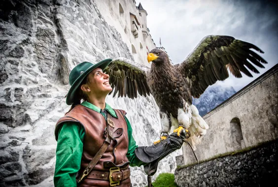 Falconiere in costume medievale con un grande aquila vicino a un muro di castello in pietra