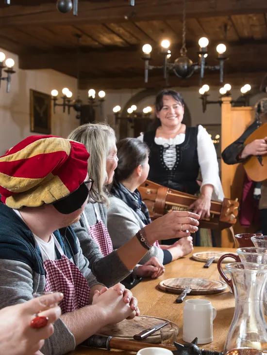 Mittelalterliches Festmahl mit Musikern und Gästen in traditioneller Kleidung in schummrigem Saal