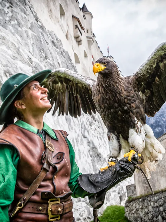 Falconer in medieval costume holding a large eagle near a stone castle wall