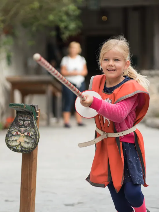 Smiling girl in medieval costume playing a jousting game at a historical festival