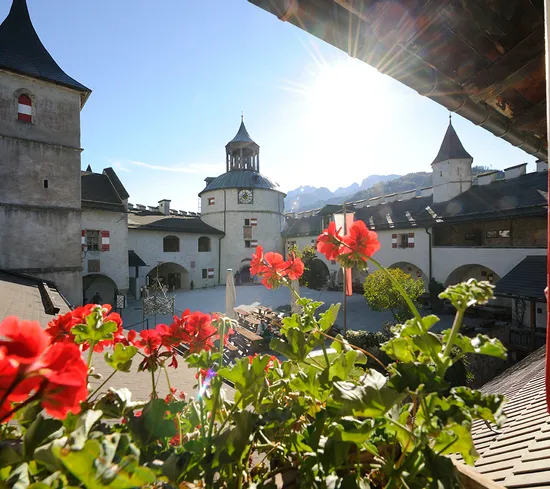 Historischer Innenhof der Burg Hohenwerfen mit roten Geranien und sonnigem Turm