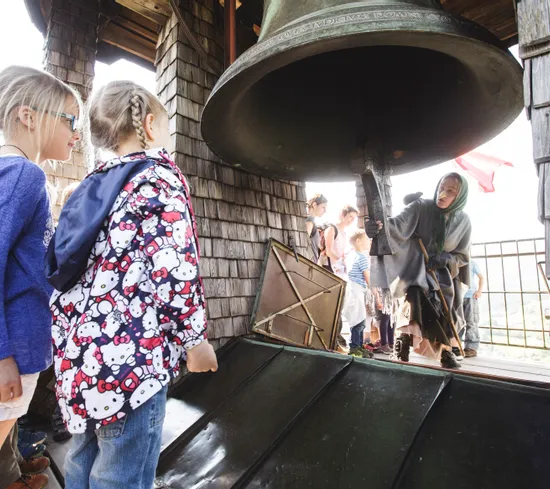 Children watching a woman ring a large tower bell during a guided tour