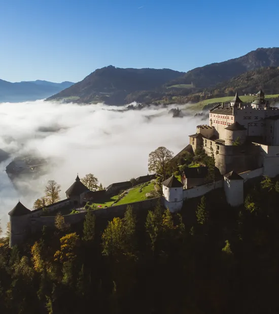 Mittelalterliche Burg auf einem Hügel mit Blick auf nebliges Tal und bewaldete Berge