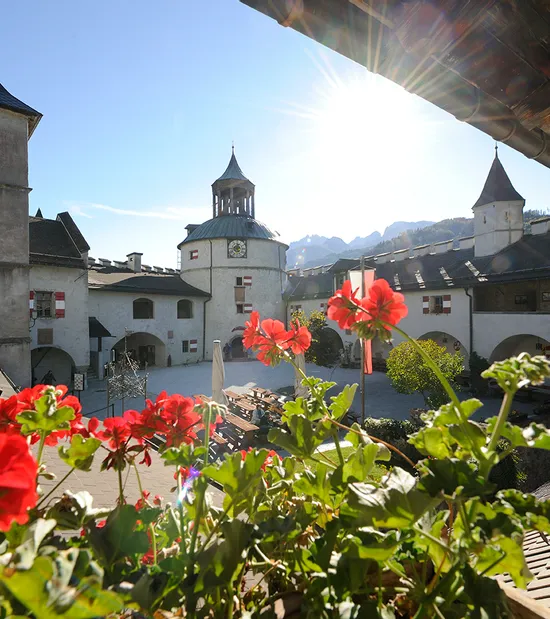 Cortile storico del castello di Hohenwerfen con gerani rossi e torre illuminata dal sole