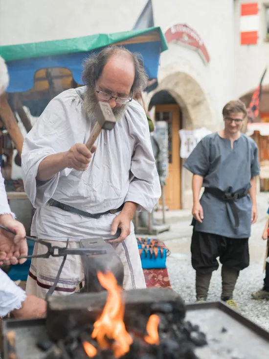Fabbri dimostrano forgiatura tradizionale in un mercato medievale con bambini spettatori