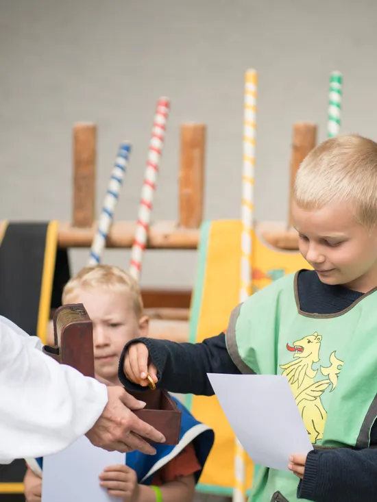 Boy in medieval costume receiving certificate during themed event with children