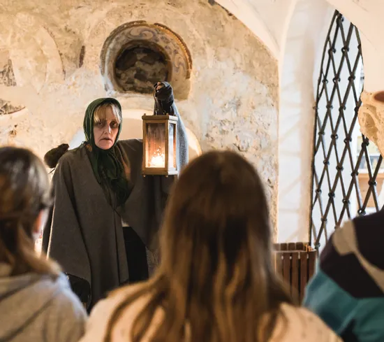 Tour guide in medieval costume holding lantern during historical tour in stone-walled room