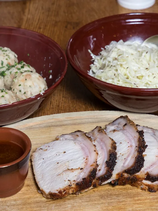Scheiben Schweinebraten mit Soße, Knödel und Sauerkraut in Schalen