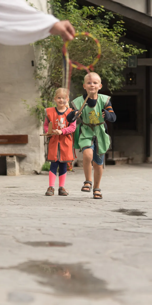 Children in medieval costumes playing a traditional outdoor game in a stone courtyard