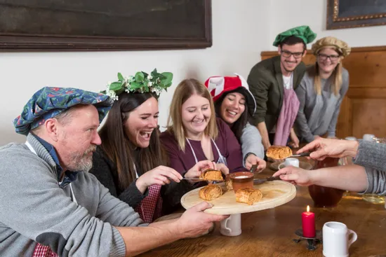 Group of people in medieval costumes sharing pastries and dipping sauce at a rustic table