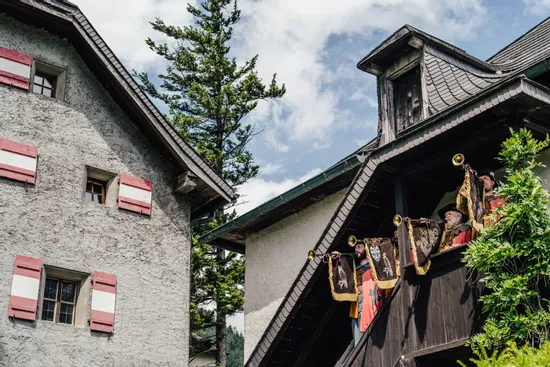 Men in traditional costumes playing herald trumpets on a wooden balcony in Alpine village