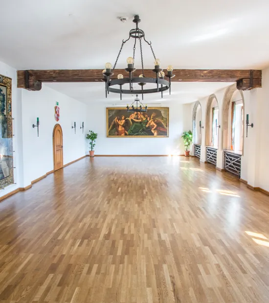 Historischer Festsaal mit Holzboden, Kronleuchtern, Rundbogenfenstern und klassischen Wandgemälden