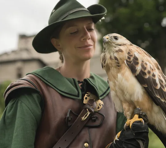 Falknerin in mittelalterlichem Kostüm mit hellbraunem Greifvogel bei historischem Burg-Event
