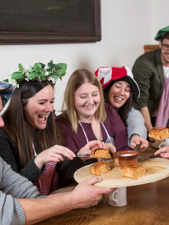 Group of people in medieval costumes sharing pastries and dipping sauce at a rustic table