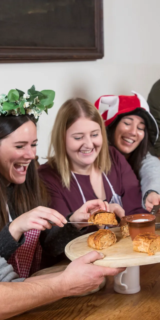 Group of people in medieval costumes sharing pastries and dipping sauce at a rustic table