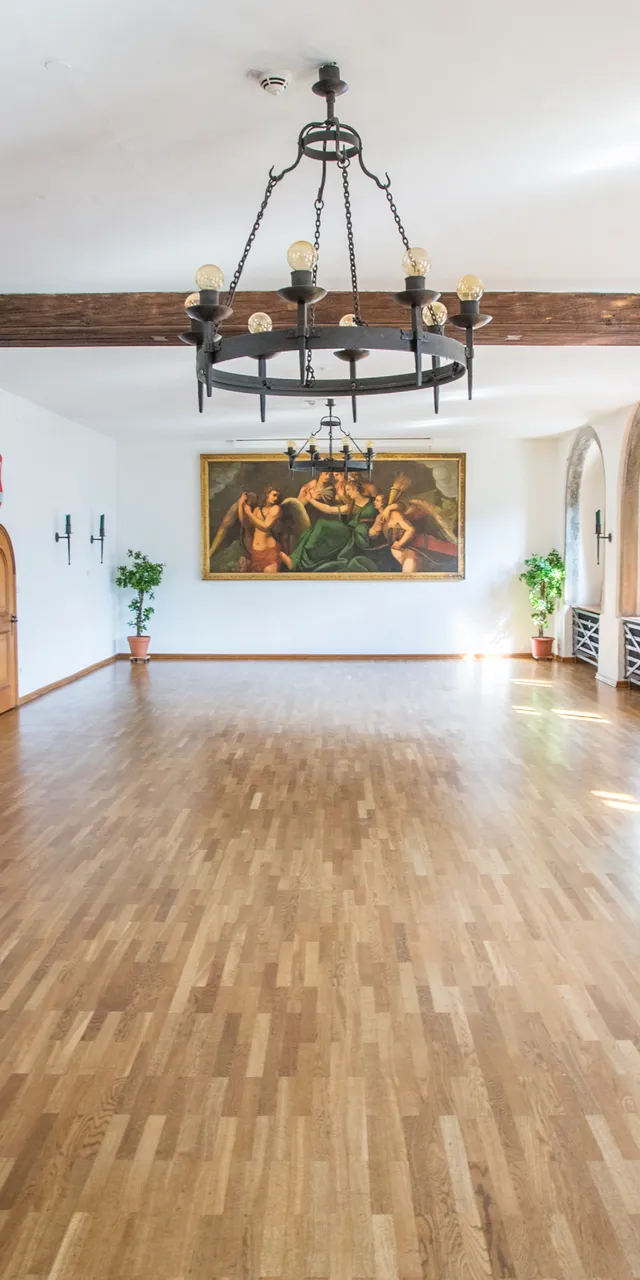 Historischer Festsaal mit Holzboden, Kronleuchtern, Rundbogenfenstern und klassischen Wandgemälden