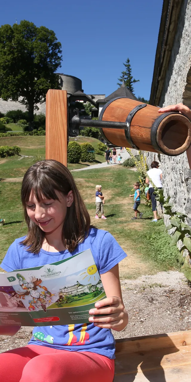 Kinder spielen nahe einer mittelalterlichen Festung, eines liest eine Karte, ein anderes schaut durch ein Holzfernrohr