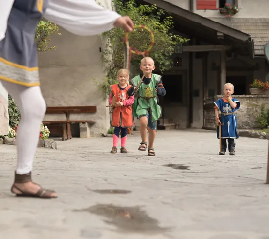 Children in medieval costumes playing a traditional outdoor game in a stone courtyard