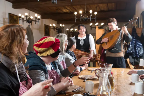 Banchetto medievale con musicisti e ospiti in abiti tradizionali in una sala scarsamente illuminata