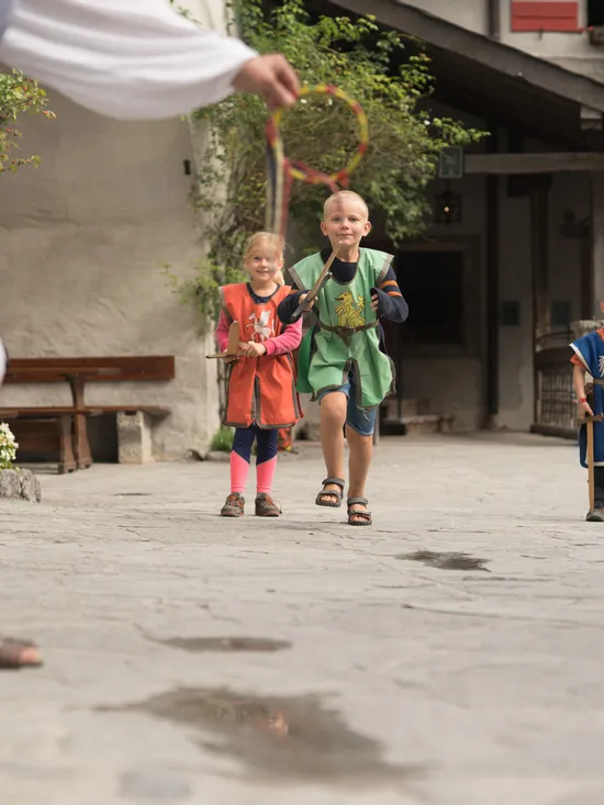 Children in medieval costumes playing a traditional outdoor game in a stone courtyard