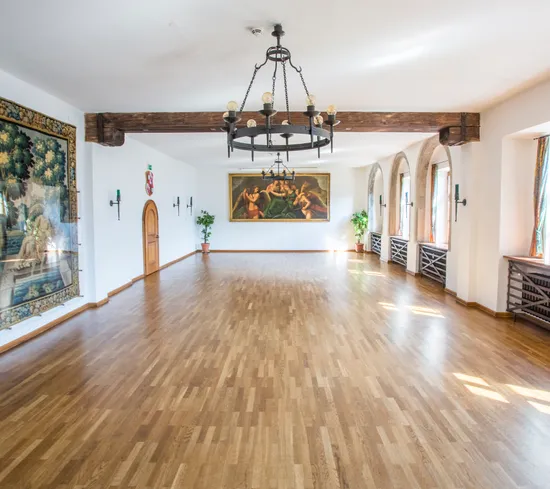 Historic banquet hall with wooden floor, chandeliers, arched windows and classical wall paintings